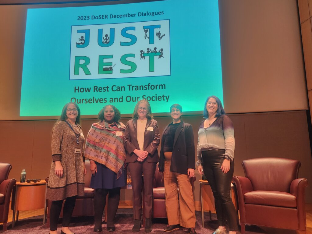 Image of 5 people standing in front of chairs, small tables, and a slide that reads "Just Rest: How Rest Can Transform Ourselves and Society." The people include, from left, DoSER Program Director Katy Hinman, Dayna Johnson, Judith Shulevitz, Dom Chatterjee and moderator Rachel Kline